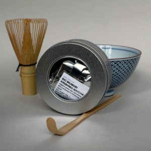 Set of a tub of ceremonial grade matcha green tea, a bamboo whisk, a bamboo stirring stick and a teacup
